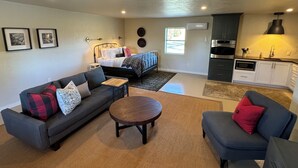 A compact living space with a sofa, a round coffee table, a bed, and a kitchenette.