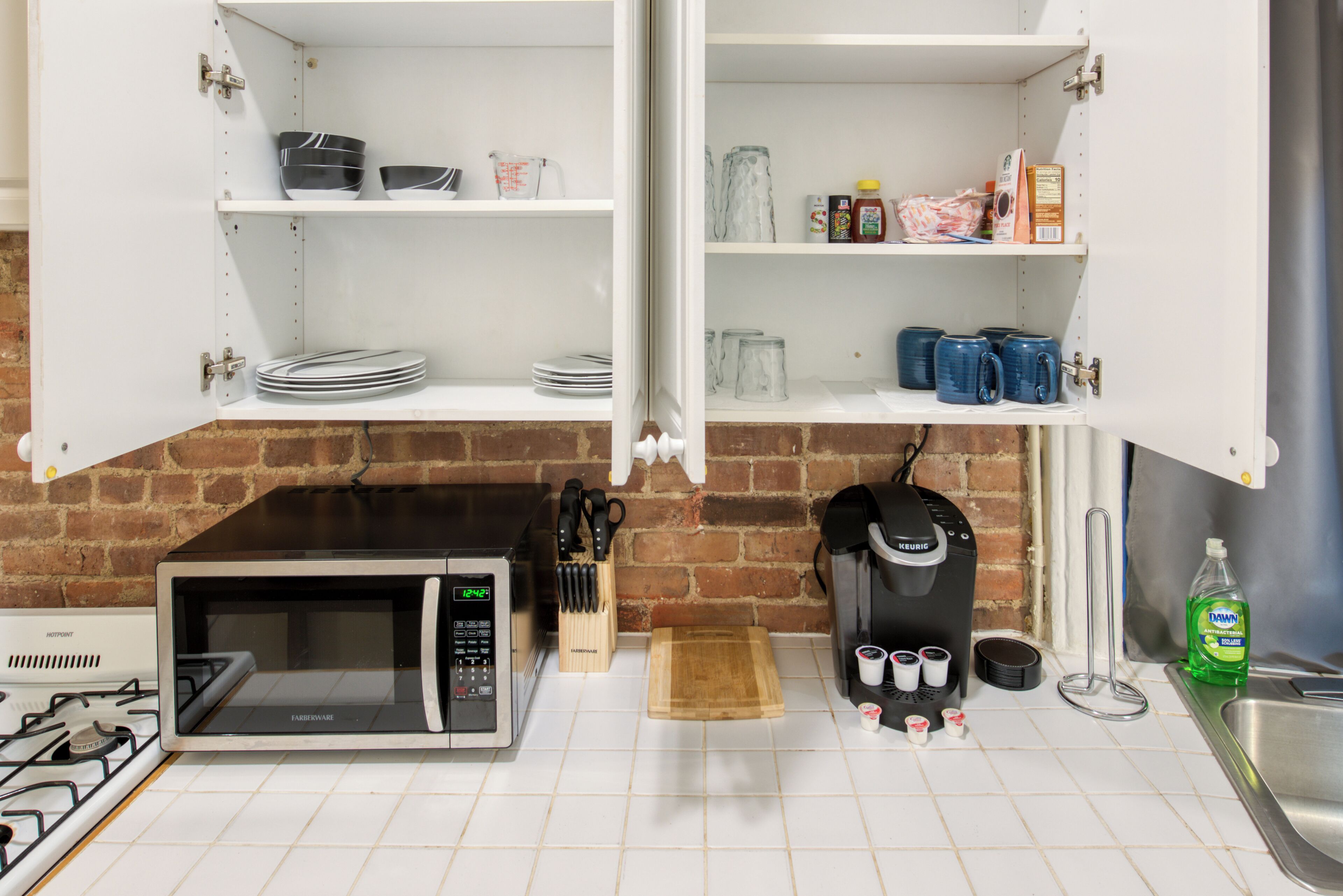 Una cocina con microondas, cafetera y utensilios sobre la encimera.