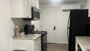 Una cocina con armarios blancos, un refrigerador negro, un bote de basura de acero inoxidable y un microondas.