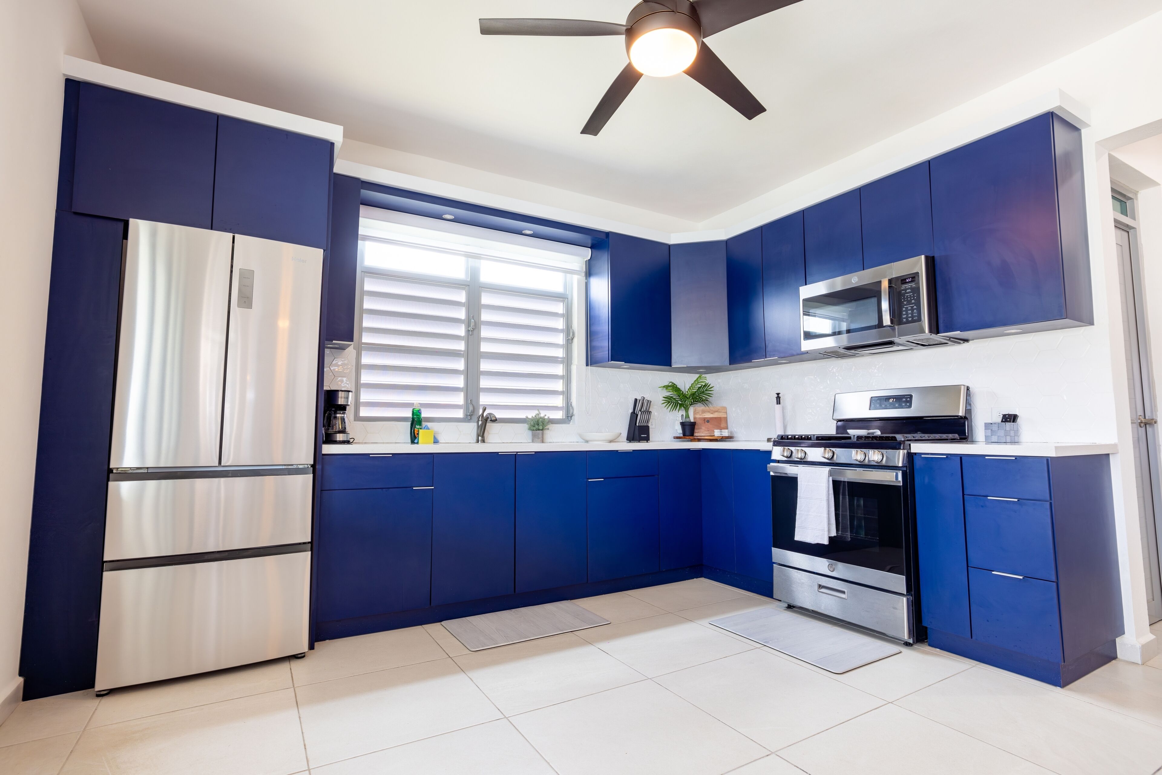Une cuisine moderne avec des armoires bleues, des appareils en acier inoxydable et un ventilateur de plafond.