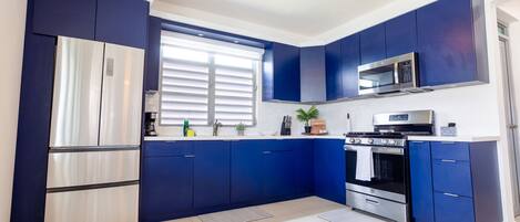 Une cuisine moderne avec des armoires bleues, des appareils en acier inoxydable et un ventilateur de plafond.