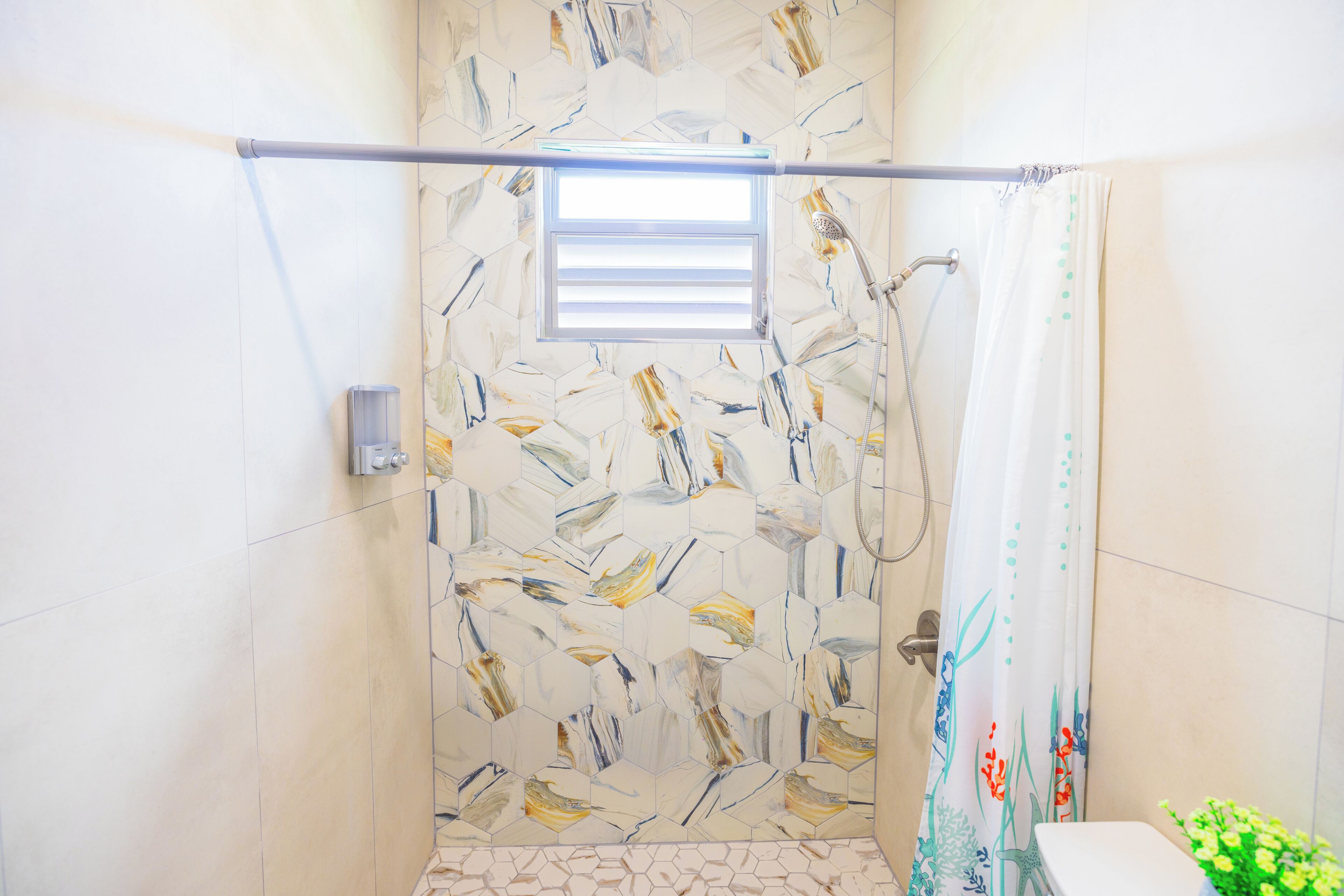 Un espace douche doté d’une porte en verre, d’une fenêtre située au-dessus de la douche et de toilettes agrémentées d’une plante verte à proximité.