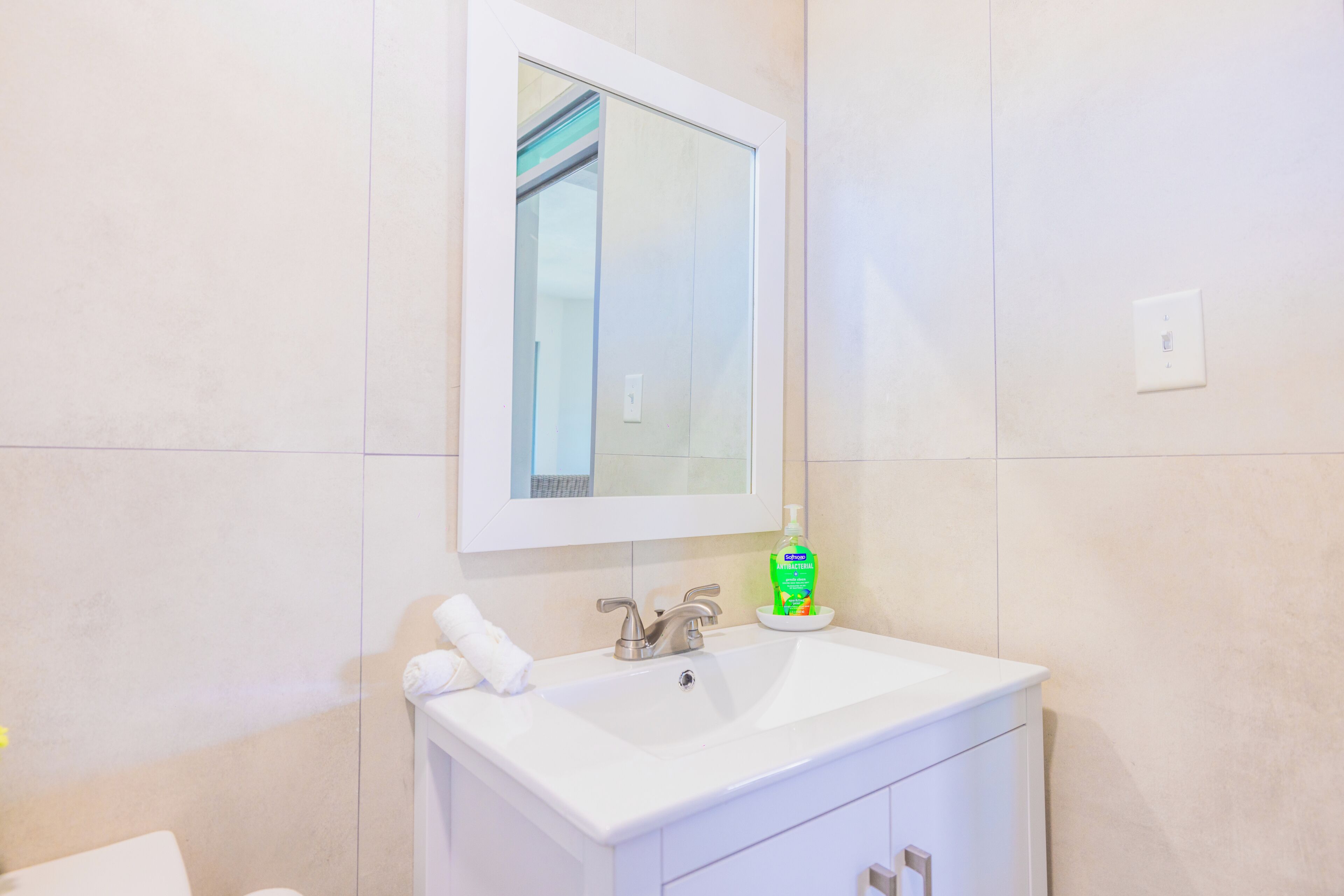 A bathroom with a white sink, a mirror, and a bottle of hand soap.