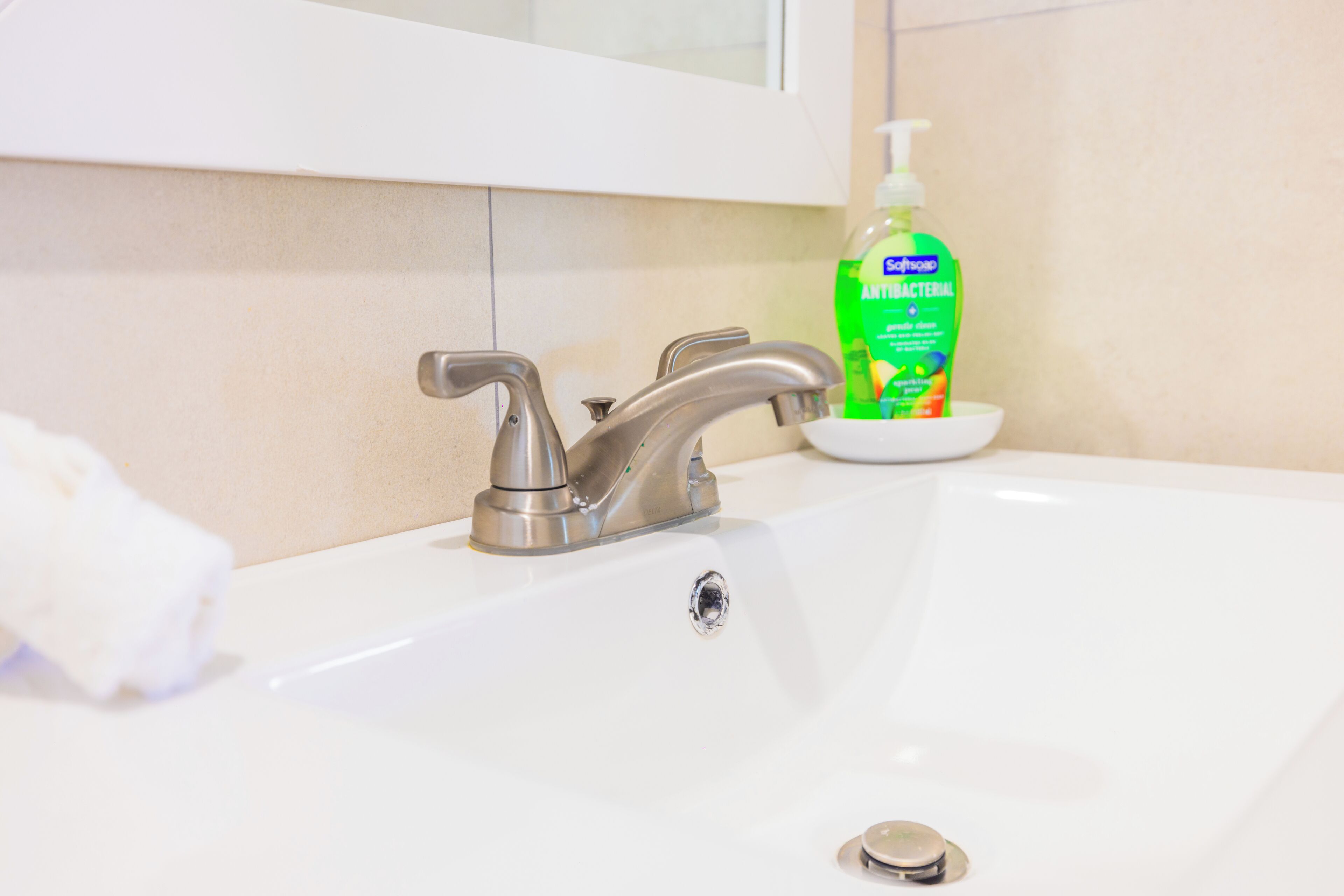 Un lavabo da bagno con un moderno rubinetto, un dispenser di sapone e un asciugamano bianco a sinistra.