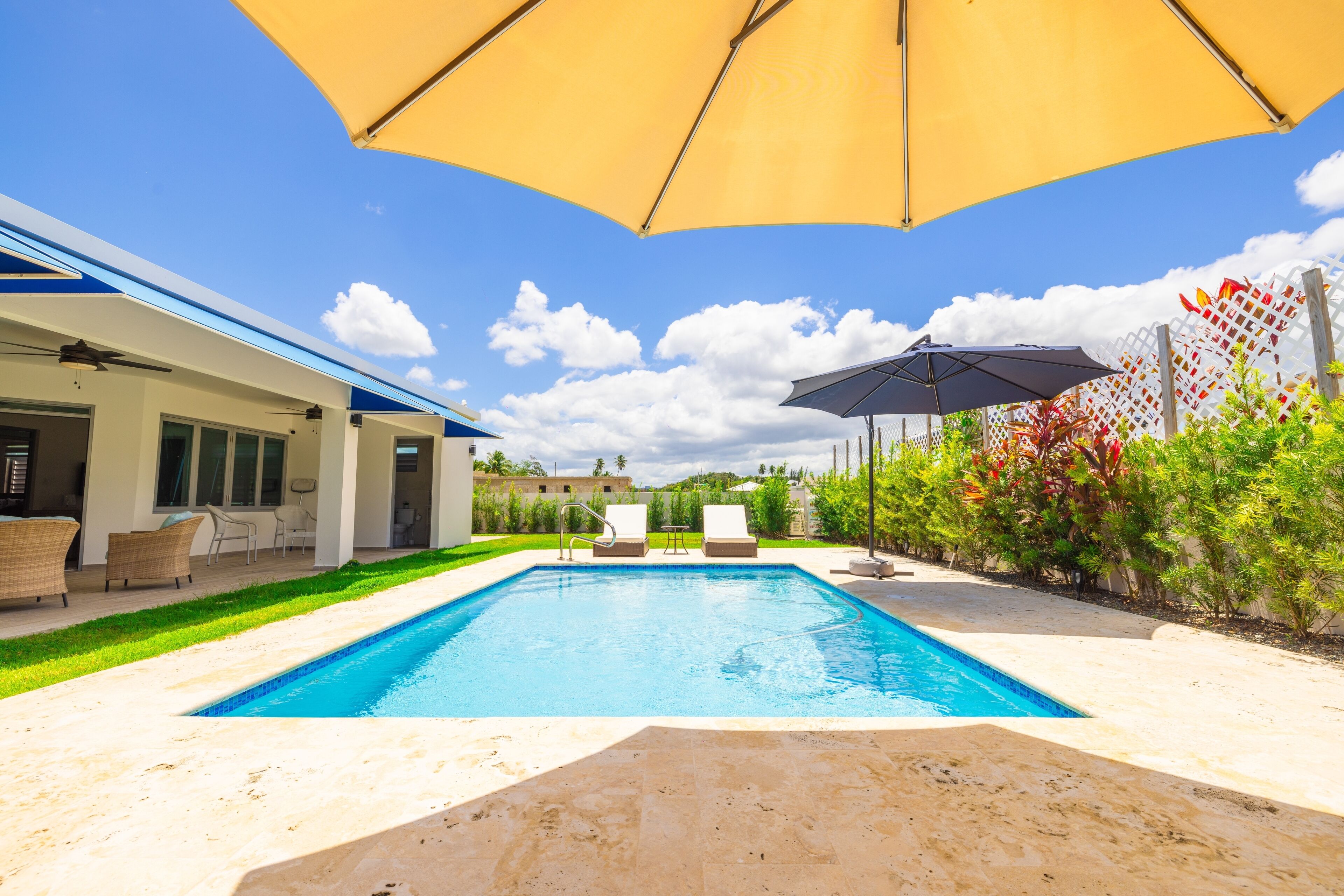 A swimming pool with lounge chairs and umbrellas, surrounded by a well-maintained lawn and a building with large windows.