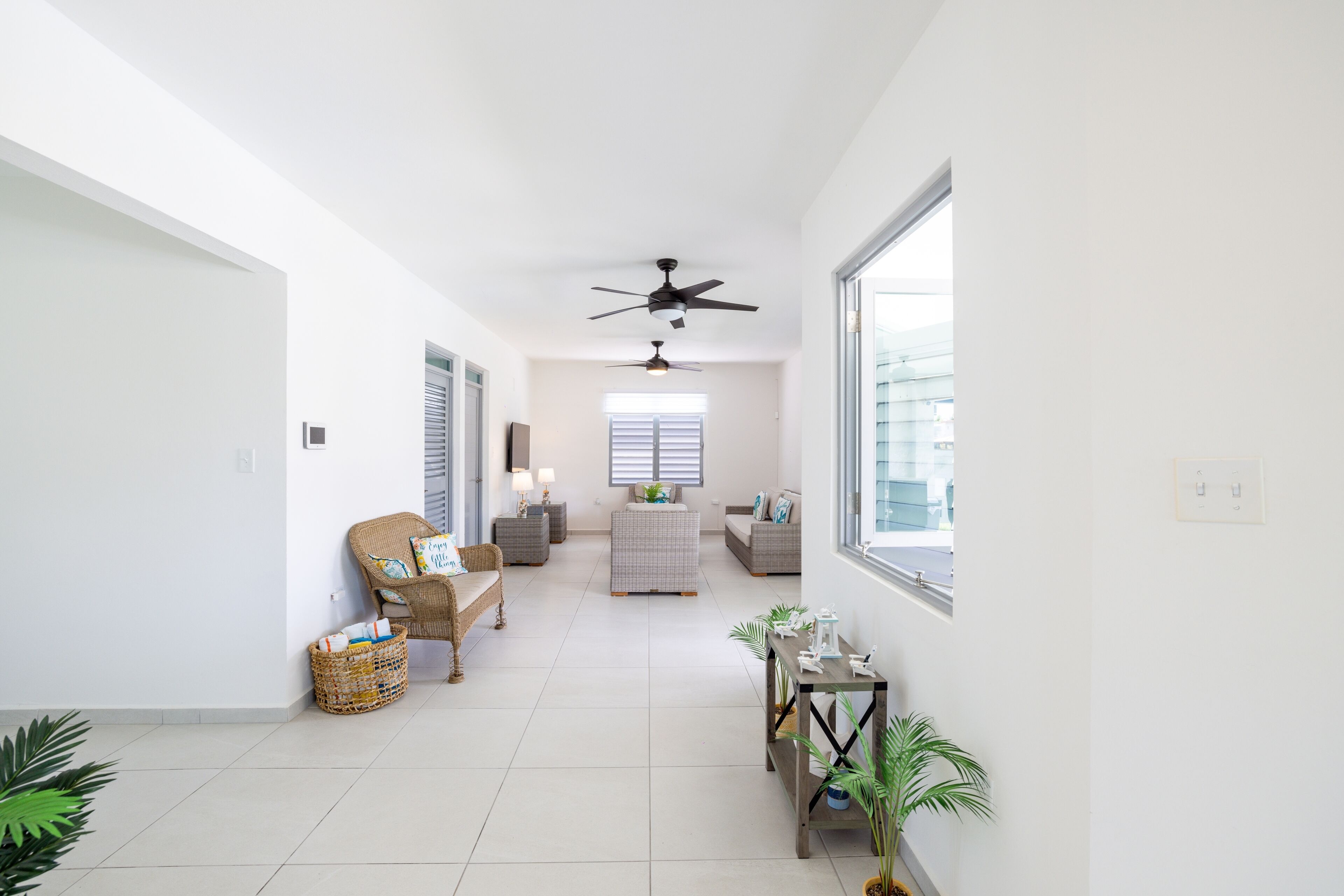 A spacious hallway with a ceiling fan, wicker furniture, and potted plants.