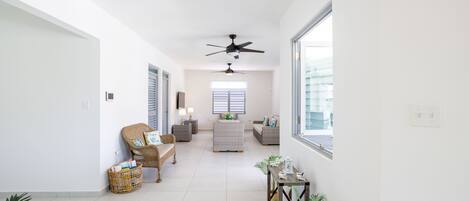 A spacious hallway with a ceiling fan, wicker furniture, and potted plants.