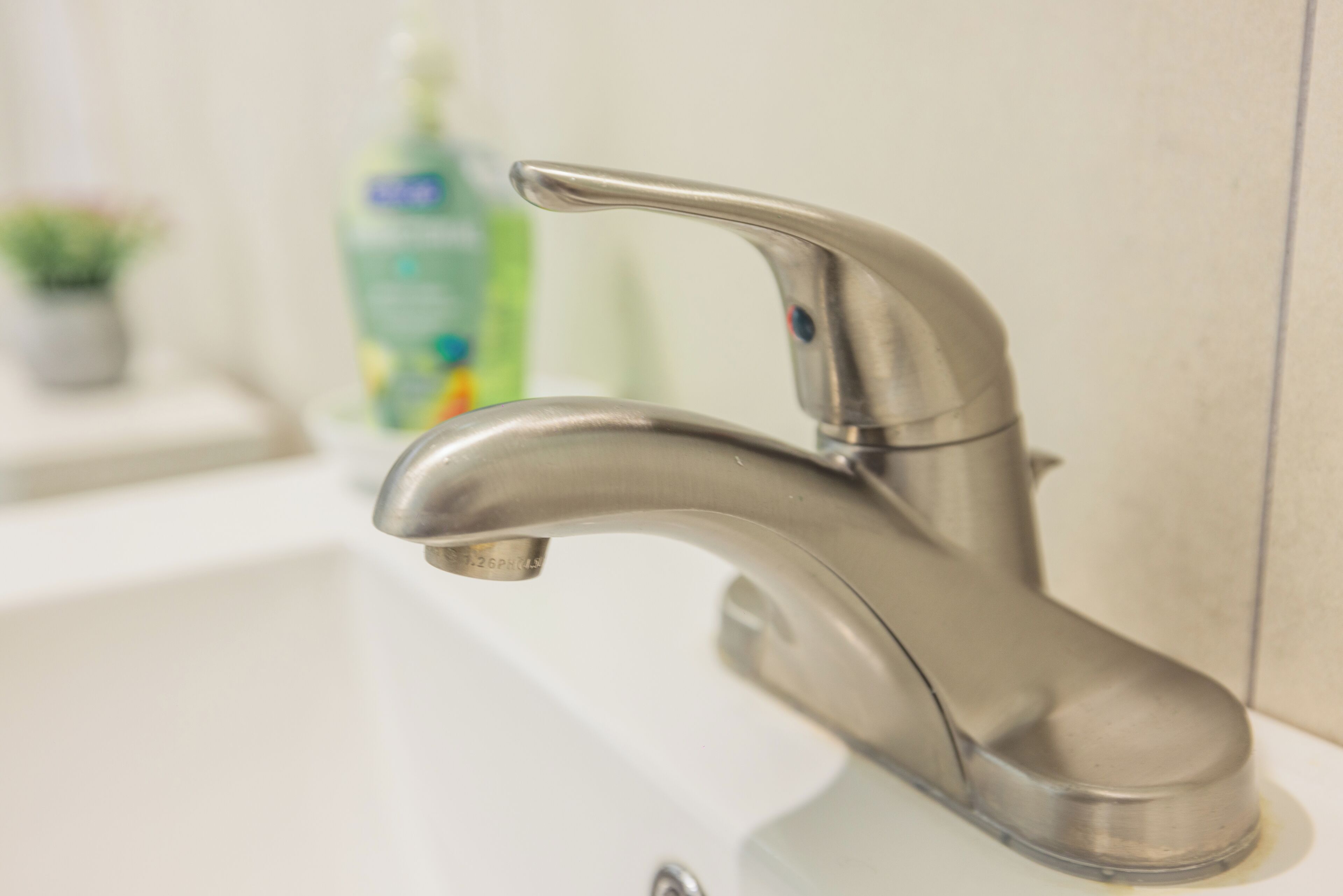 A modern bathroom with a chrome faucet, a white sink, and a green bottle of hand soap in the background.