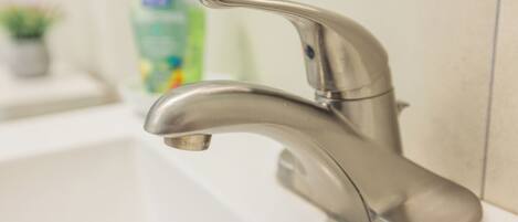 A modern bathroom with a chrome faucet, a white sink, and a green bottle of hand soap in the background.