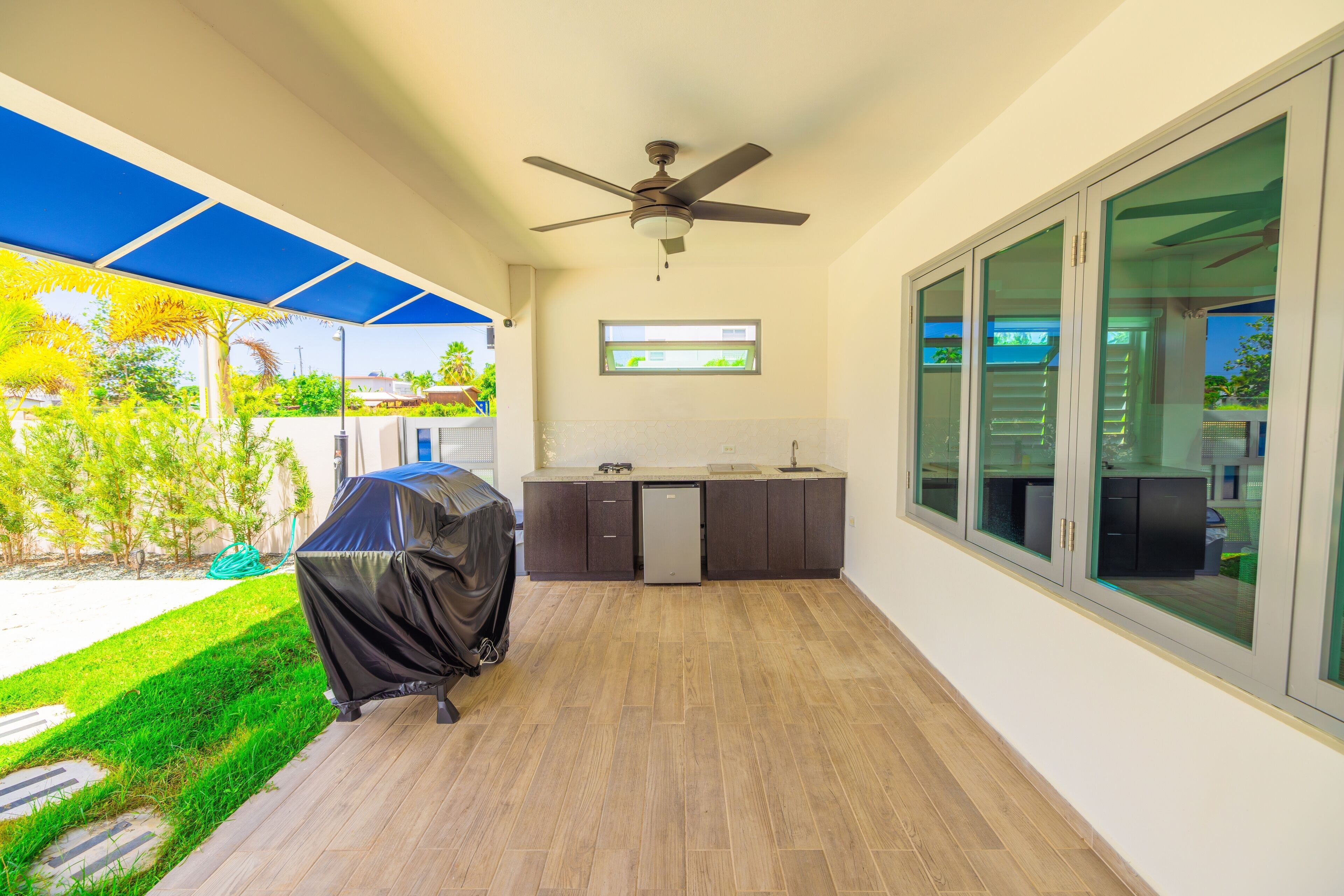 A covered patio with a ceiling fan, a barbecue grill, and a kitchen area with a dishwasher and cabinets.