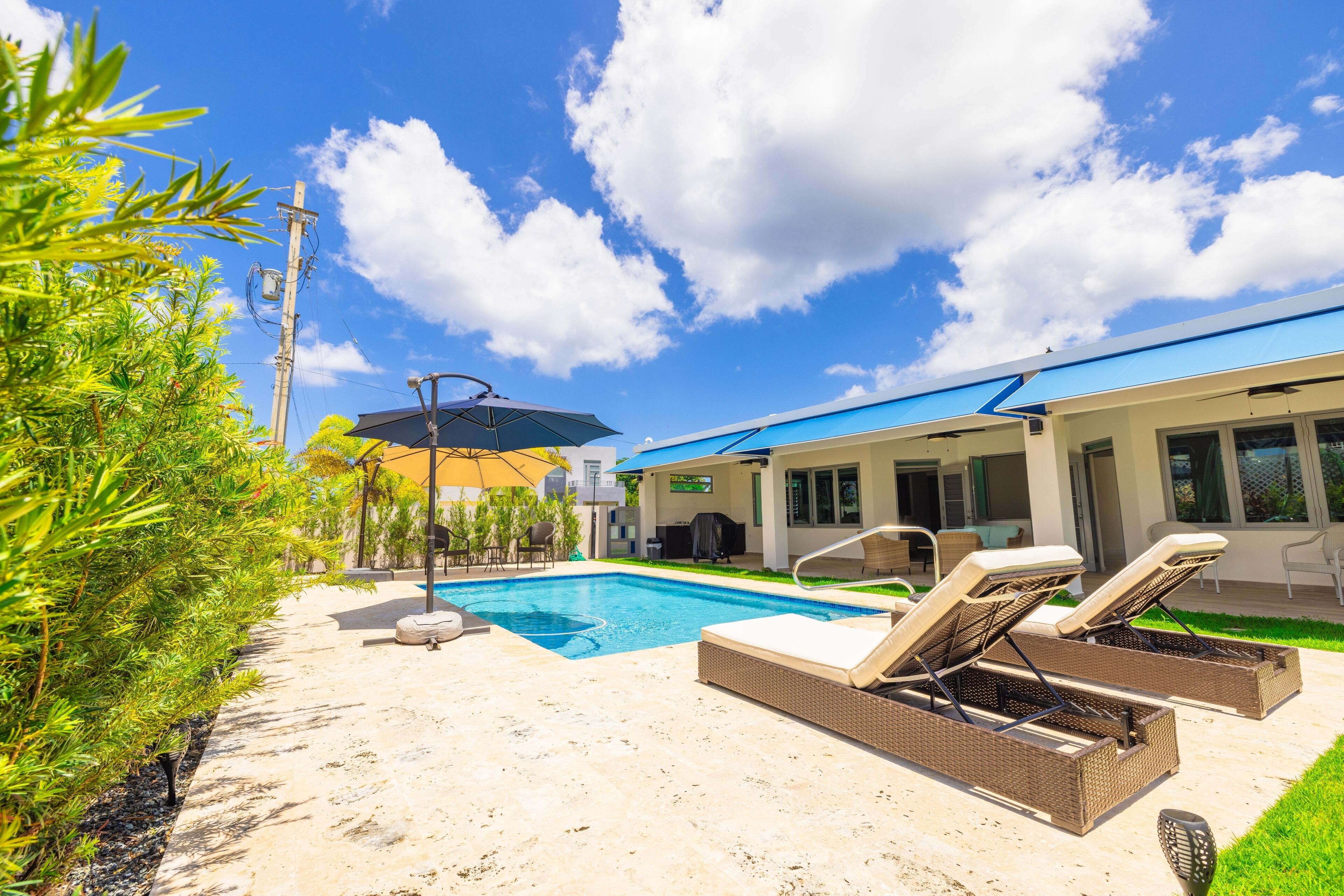 A swimming pool with lounge chairs, a covered patio area, and a building with large windows.