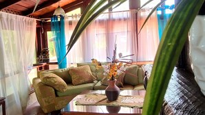 Un salon chaleureux avec un plafond en bois, un canapé vert, une table basse ornée d’un vase de fleurs et une grande plante au premier plan.