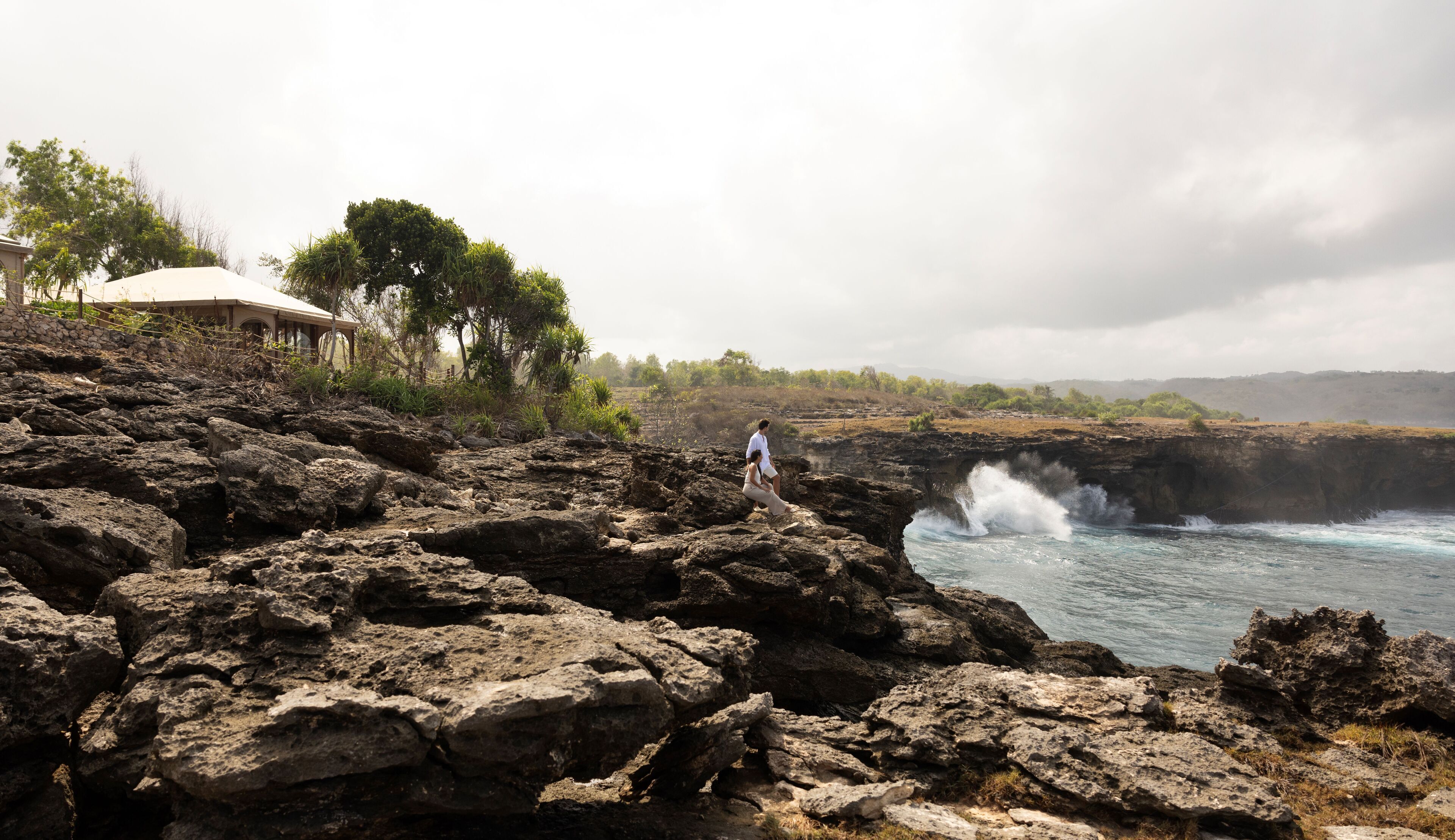 A rocky coastal landscape with a man and a woman standing on a cliff overlooking the ocean.