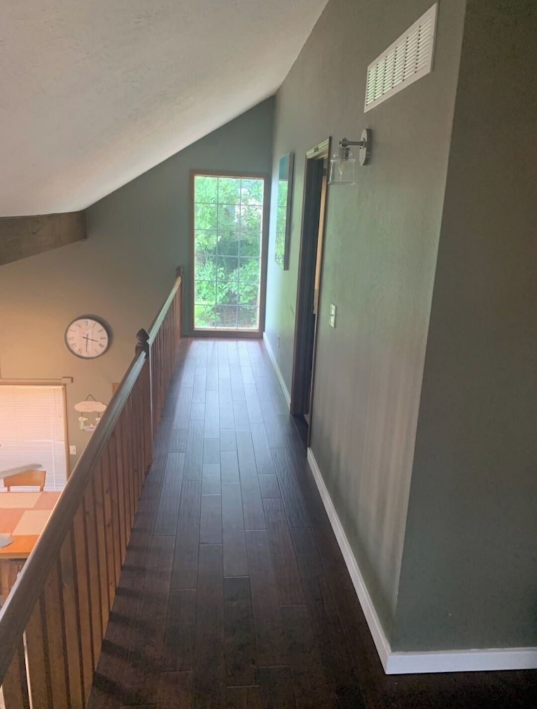 A narrow hallway with wooden flooring, a clock on the left, and a door on the right.