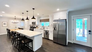 Une cuisine moderne dotée d’un îlot central, de luminaires suspendus et d’un réfrigérateur en acier inoxydable.