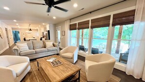 Un salon spacieux avec une grande fenêtre, un ventilateur de plafond et une table basse en bois.
