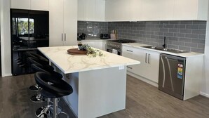 A modern kitchen with white cabinets, a marble countertop, a stainless steel refrigerator, and a black tiled backsplash.