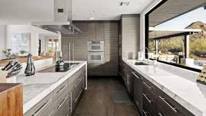 Una cocina moderna con una isla central, hornos integrados y un amplio ventanal con vistas a un paisaje desértico.