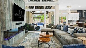 Amplia sala de estar con chimenea moderna, un amplio conjunto de sofás y una cocina visible a través de un vano abierto.
