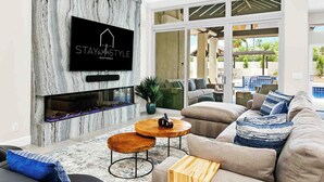 Una sala de estar moderna con una pared de piedra, un televisor de pantalla plana, chimenea, vista a la piscina y un área de estar confortable.
