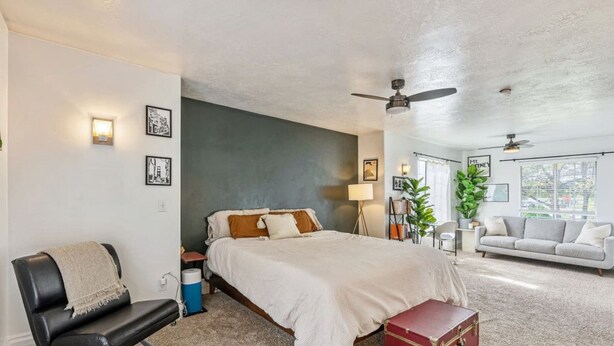 A bedroom with a bed, a chair, a suitcase, a ceiling fan, and a window.