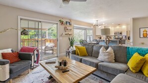 A spacious living room with a grey sofa, a wooden coffee table, and a sliding glass door leading to a balcony.