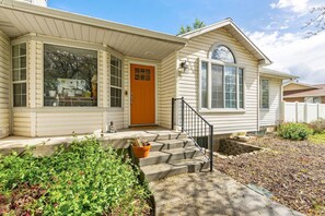 A single-story house with a front porch, a front door, and a small front yard with a potted plant and steps leading to the door.