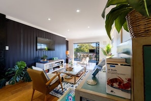 A modern living room with a flat-screen TV, a bookshelf, a coffee table, and a dining area.
