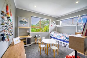 Quarto compacto com cama, escrivaninha, cadeira, mesinha e janela com vista para o verde.