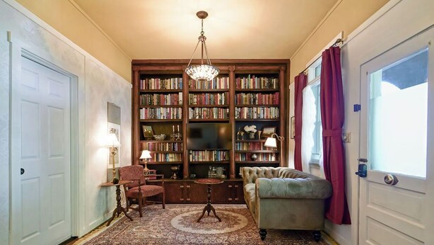 Een knusse woonkamer met een grote boekenkast, een comfortabele bank en een vloerkleed.