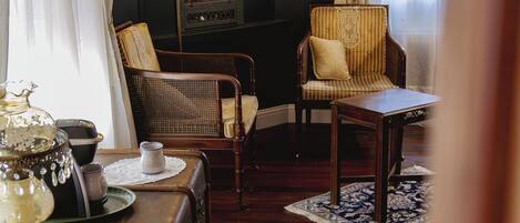 A room with two wicker chairs, a wooden table, a vintage lamp, and a large mirror on the wall.