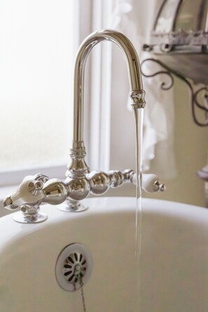 Ein Wasserhahn im Vintage-Stil, aus dem Wasser in ein weißes Waschbecken fließt.