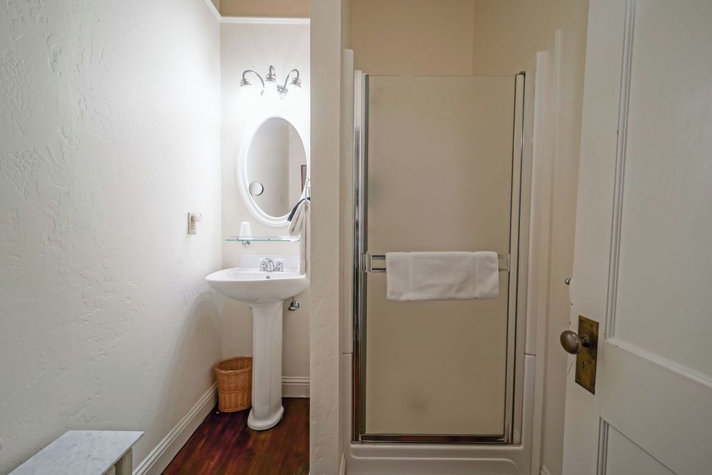 A bathroom with a pedestal sink, a mirror, a shower with a glass door, and a towel hanging on the door.