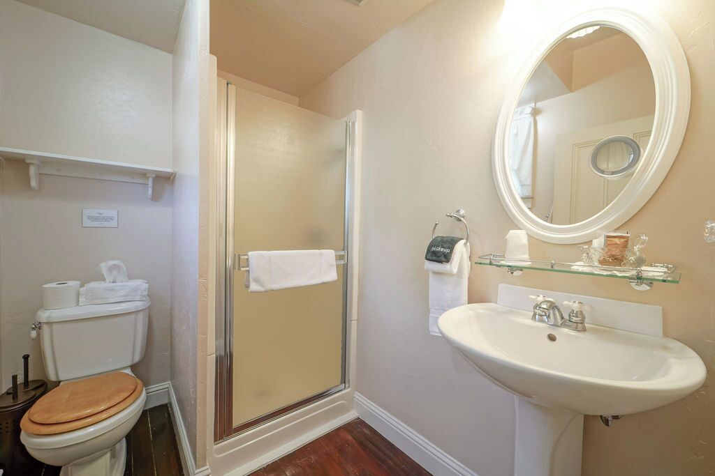 A bathroom with a toilet, shower, sink, and mirror.