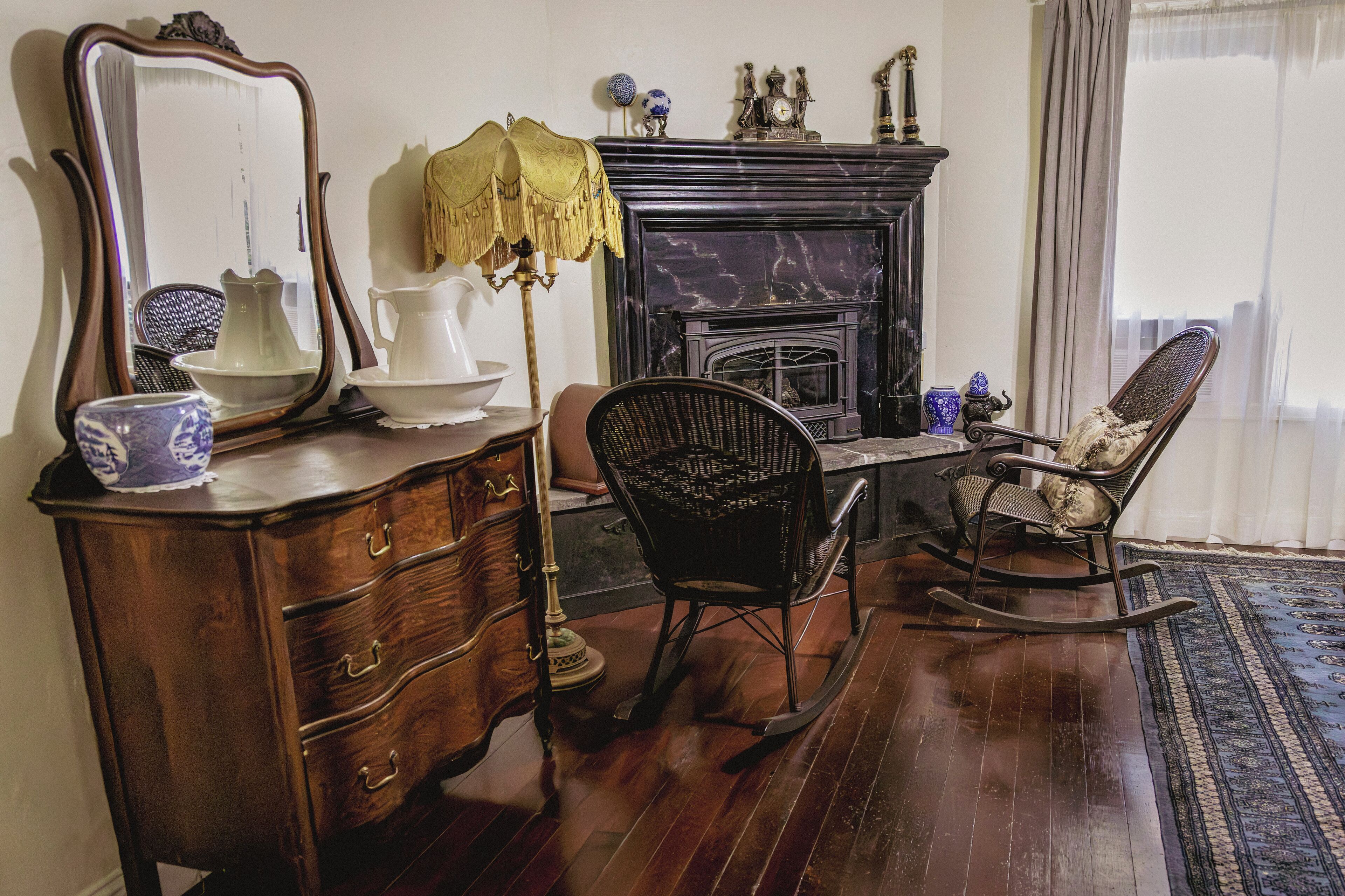 A traditional room with a wooden dresser, a rocking chair, a fireplace, and a large mirror.