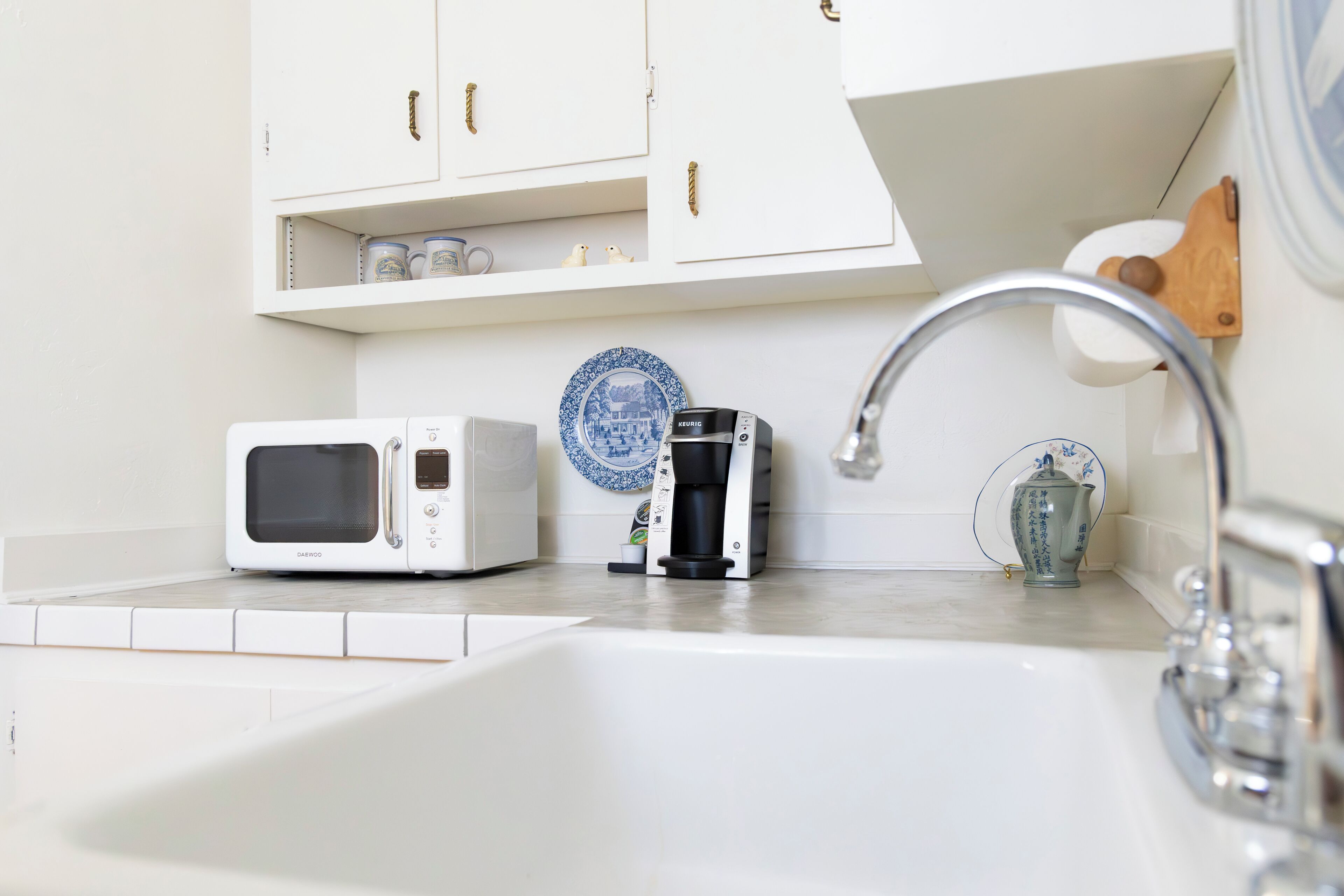 A kitchen with white cabinets, a white microwave, a coffee maker, and a sink with a faucet.