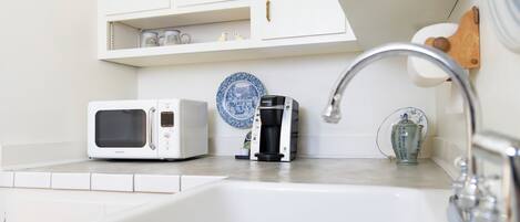 A kitchen with white cabinets, a white microwave, a coffee maker, and a sink with a faucet.