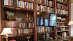 Une bibliothèque avec des étagères en bois remplies de livres, un téléviseur et des objets de décoration.