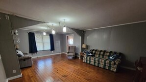 A spacious living room with hardwood flooring, a plaid sofa, a patterned armchair, and a small table with a lamp. - Charming 3-bedroom house in tranquil Oraville minutes from  Kinkaid Lake.   (Oraville)