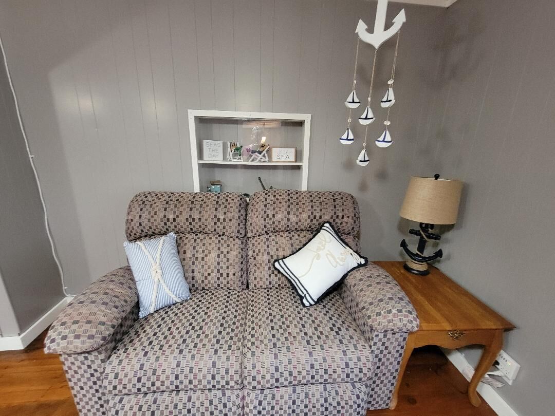 Ein gemustertes Sofa mit Kissen, ein Holztisch mit Lampe und ein Wandregal mit Dekoration.