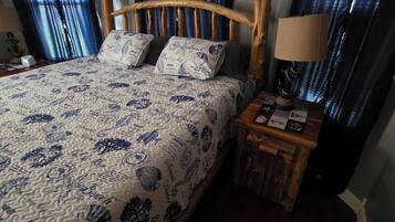 Un lit avec une couvre-lit à motifs, une tête de lit en bois, deux oreillers, une table de chevet avec une lampe et une fenêtre avec des rideaux.