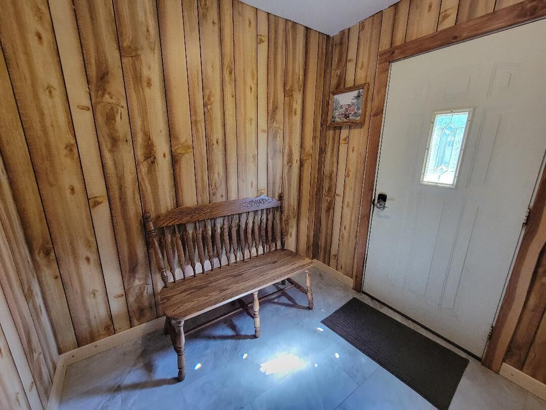 A wooden bench in a room with vertical wooden paneling and a door with a window.
