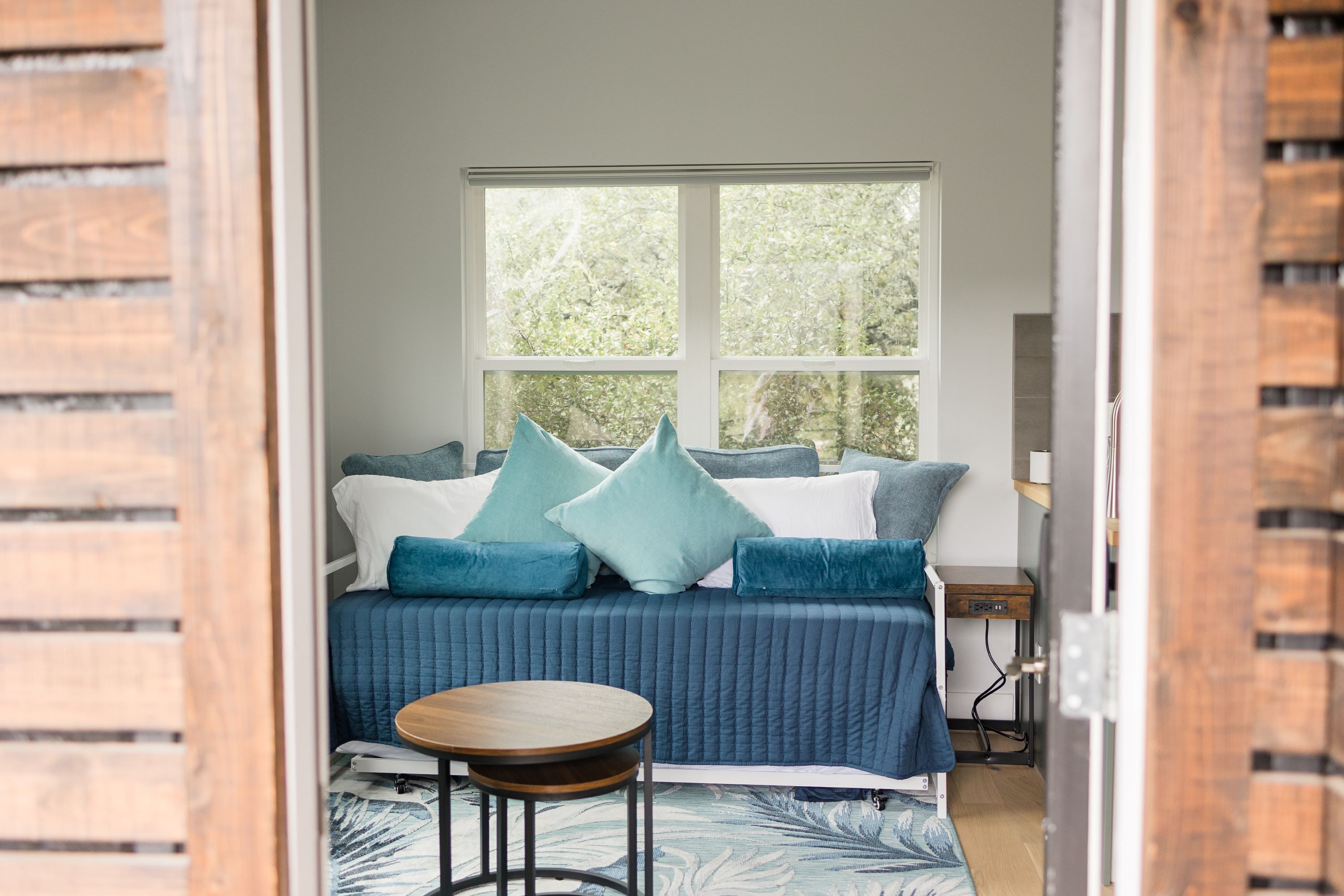 Una habitación acogedora con un sofá azul, una mesita de madera y una ventana con vistas a la vegetación.