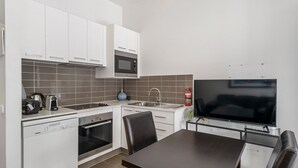 A compact kitchen with white cabinets, a microwave, a sink, and a built-in oven. There's a flat-screen TV mounted on the wall and a small dining table with chairs. - Hangar - Dinner plain (Dinner Plain)