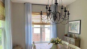 A dining area with a wooden table, white chairs, a chandelier, and a vase with flowers. - Rooted Lake Cottage w/ Golf Cart - NEW to VRBO! (Tullahoma)