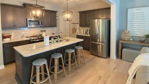 A modern kitchen with a central island, bar stools, stainless steel appliances, and pendant lighting. - Rooted Lake Cottage w/ Golf Cart - NEW to VRBO! (Tullahoma)