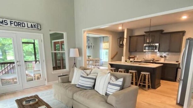 A modern living room with a sofa, coffee table, and a view of a kitchen and dining area. - Rooted Lake Cottage w/ Golf Cart - NEW to VRBO! (Tullahoma)
