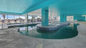 Une piscine intérieure avec des bords carrelés, des chaises longues et une vue sur l’extérieur.
