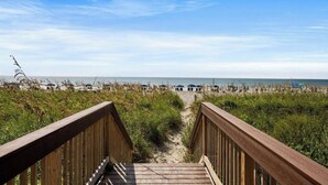 Une promenade en bois menant à une plage où l’on trouve des parasols et des chaises de plage.
