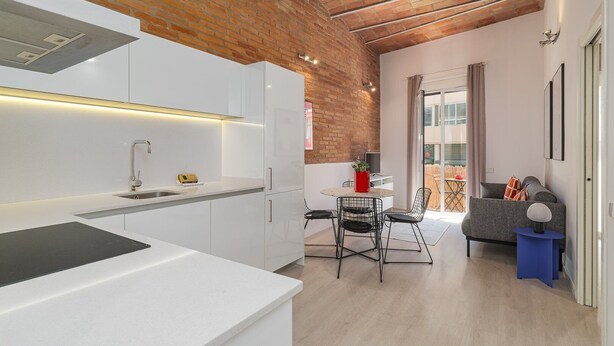 A modern kitchen with white cabinets, a built-in stove, and a dining area with a round table and chairs. - GuestReady - Lovely home in the heart of Barcelona (Barcelona)